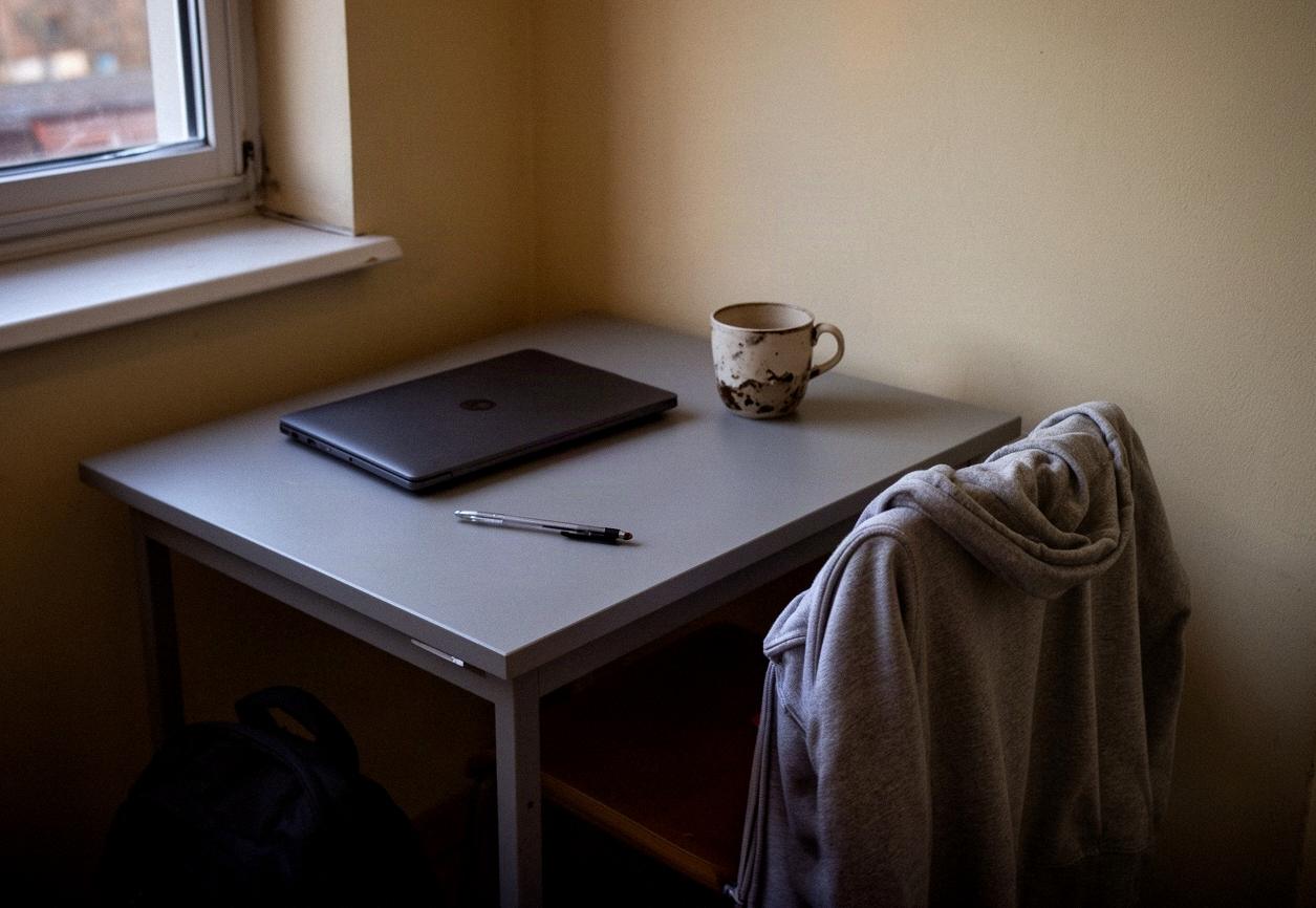 Biurko studenta w pokoju akademika z zamkniętym laptopem i kubkiem w popołudniowym świetle